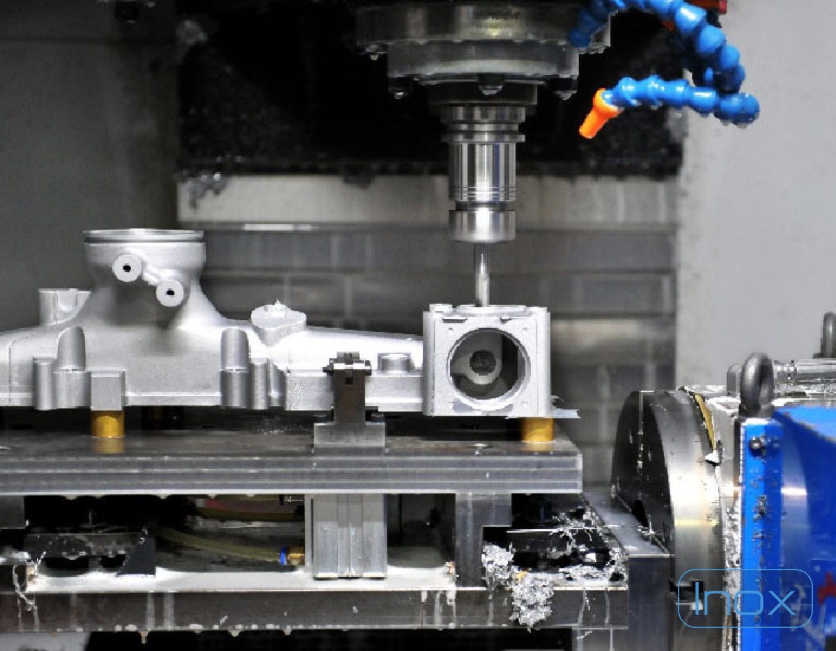 An aluminium die casting fixtured in a CNC machining cell, cutting tool engaging a bore with coolant lines and chips visible